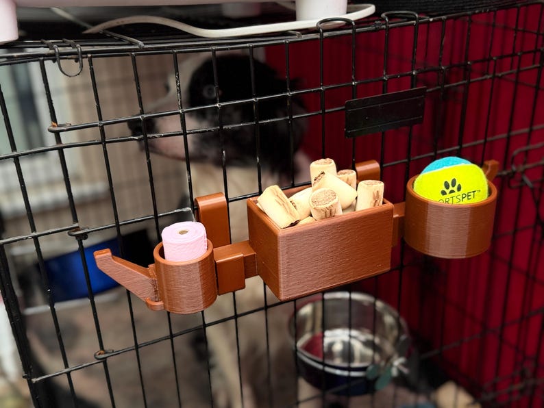 Brown PETG 3D-printed dog crate organiser for walkers and pet owners. Holds treats, tennis ball, and poo bags with slots for two leads. Heat-resistant, tool-free setup with adjustable hooks. Customisable with dog names, available in other colours.