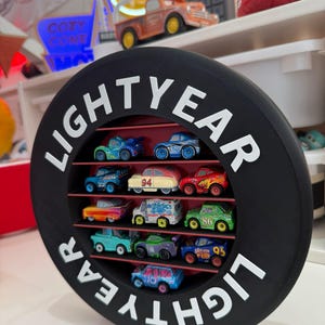 May include: A black, circular display shelf with the word "LIGHTYEAR" in white lettering. The shelf contains a collection of colorful toy cars. The cars are arranged on red shelves within the circular frame, creating a visually appealing display.