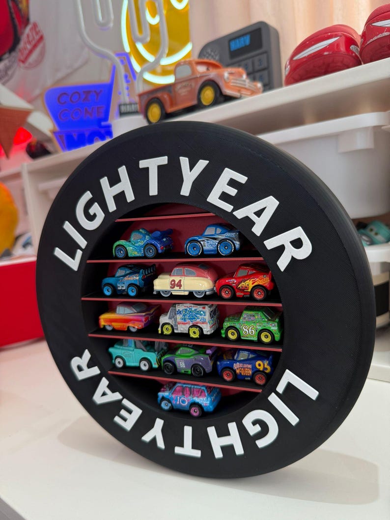 May include: A black, circular display shelf with the word "LIGHTYEAR" in white lettering. The shelf contains a collection of colorful toy cars. The cars are arranged on red shelves within the circular frame, creating a visually appealing display.