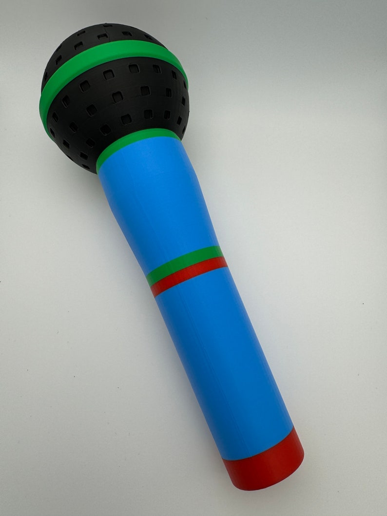 A 3D-printed, colorful plastic microphone prop held in a hand. This vibrant and durable design is perfect for photo booth props, party accessories, or as a fun kids' toy, available in various color combinations.