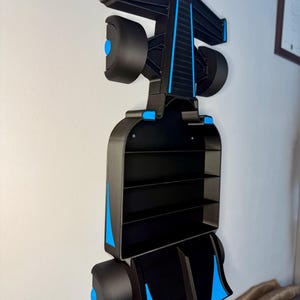 Op de afbeelding: Zwart en blauw Formule 1 raceauto-vormig wandrek. Het rek heeft meerdere compartimenten en is aan een witte muur bevestigd. Het ontwerp bevat blauwe accenten op de wielen en de carrosserie.