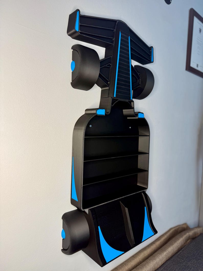 Op de afbeelding: Zwart en blauw Formule 1 raceauto-vormig wandrek. Het rek heeft meerdere compartimenten en is aan een witte muur bevestigd. Het ontwerp bevat blauwe accenten op de wielen en de carrosserie.
