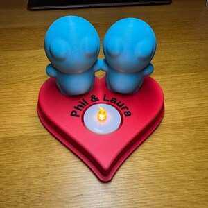 Personalised 3D printed tealight holder featuring cute bubble people figurines on a heart-shaped base. Customisable with names, perfect as a romantic Valentine’s gift, anniversary present, or home decor. Designed for use with LED tealights.