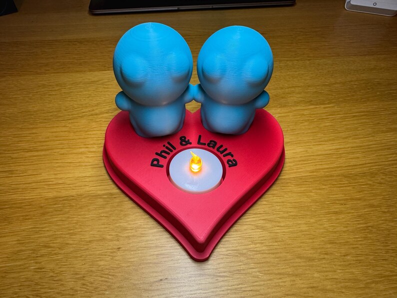 Personalised 3D printed tealight holder featuring cute bubble people figurines on a heart-shaped base. Customisable with names, perfect as a romantic Valentine’s gift, anniversary present, or home decor. Designed for use with LED tealights.