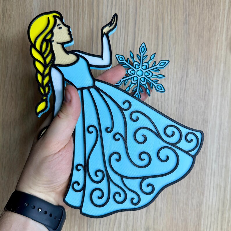 May include: A light blue cutout of a princess with a long yellow braid, wearing a blue dress with black swirl details. A blue snowflake is next to her. The princess is holding her hand up. The cutout is held by a person.
