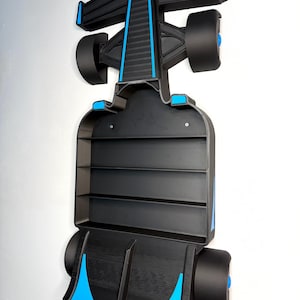 Op de afbeelding: Zwart en blauw Formule 1 raceauto wandrek. Het rek heeft drie horizontale planken en blauwe accenten. Het ontwerp omvat vleugels, wielen en andere kenmerken van een raceauto.
