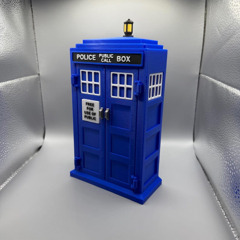 May include: A blue police box replica with white window frames and the text "POLICE PUBLIC CALL BOX" on top. The doors have a sign that reads "FREE FOR USE OF PUBLIC". A small yellow light sits on top.