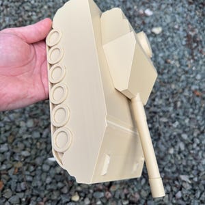 May include: A beige plastic model tank featuring a smooth, matte finish, a central turret, a long cylindrical barrel, and a series of circular wheels along the side track assembly. The structure is monochromatic with clean, angular lines.