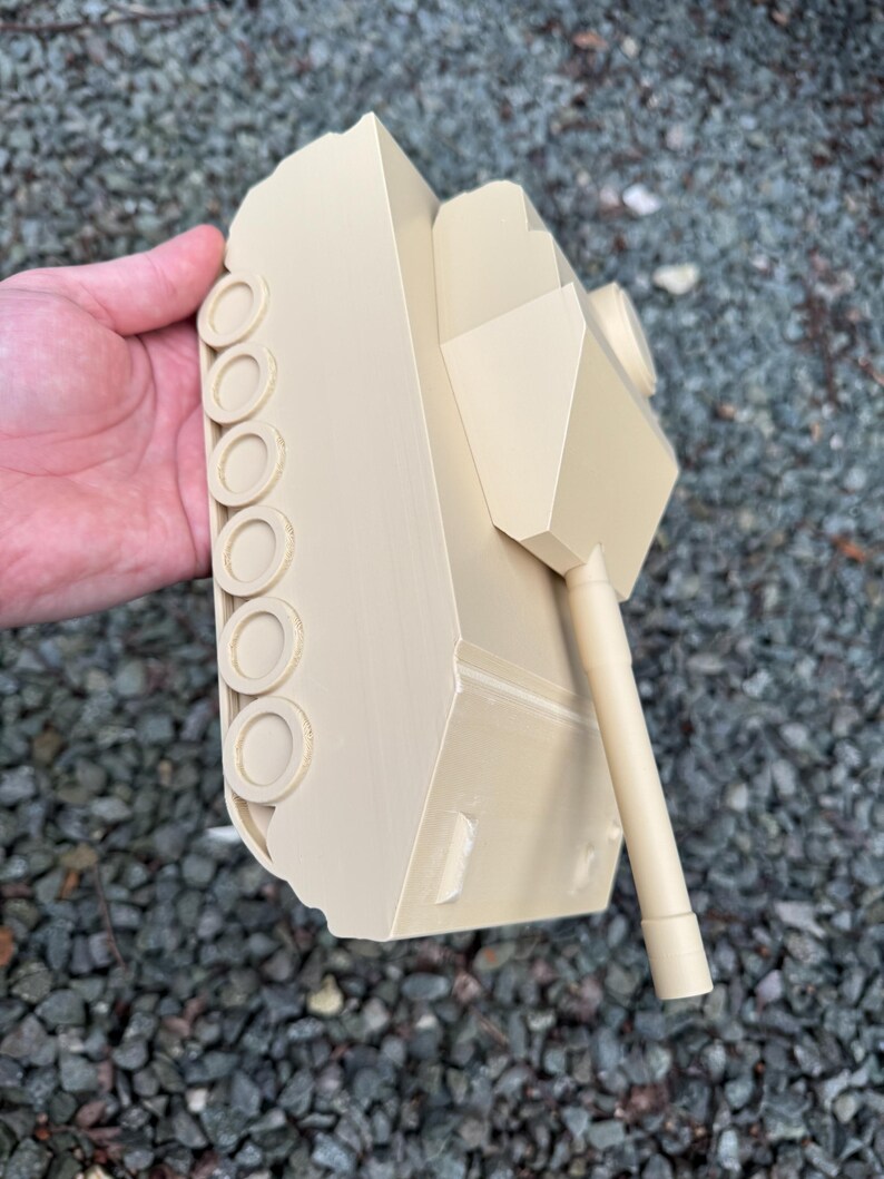 May include: A beige plastic model tank featuring a smooth, matte finish, a central turret, a long cylindrical barrel, and a series of circular wheels along the side track assembly. The structure is monochromatic with clean, angular lines.