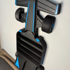 Op de afbeelding: Een zwart en blauw Formule 1 raceauto-rek, gemonteerd aan een witte muur. Het rek heeft een gedetailleerd ontwerp, inclusief wielen en een achtervleugel. Het rek is ongeveer 61 cm lang.