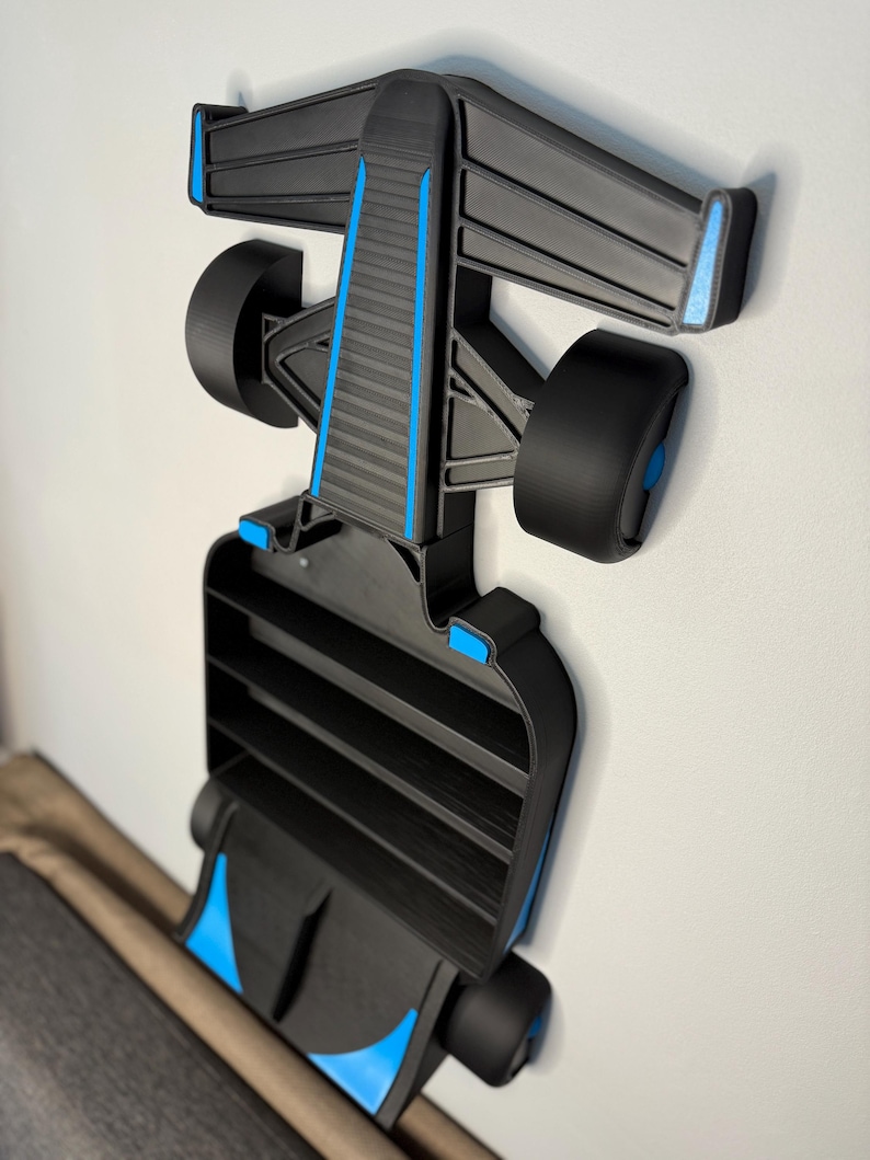 Op de afbeelding: Een zwart en blauw Formule 1 raceauto-rek, gemonteerd aan een witte muur. Het rek heeft een gedetailleerd ontwerp, inclusief wielen en een achtervleugel. Het rek is ongeveer 61 cm lang.