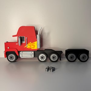 May include: A red and black toy truck with the number 95 in yellow. The truck has a trailer and several small silver pieces are in front of the truck.