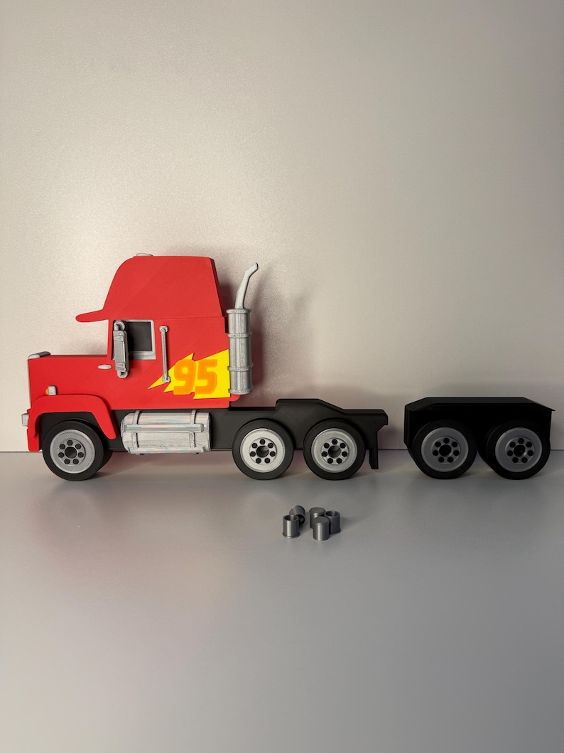 May include: A red and black toy truck with the number 95 in yellow. The truck has a trailer and several small silver pieces are in front of the truck.