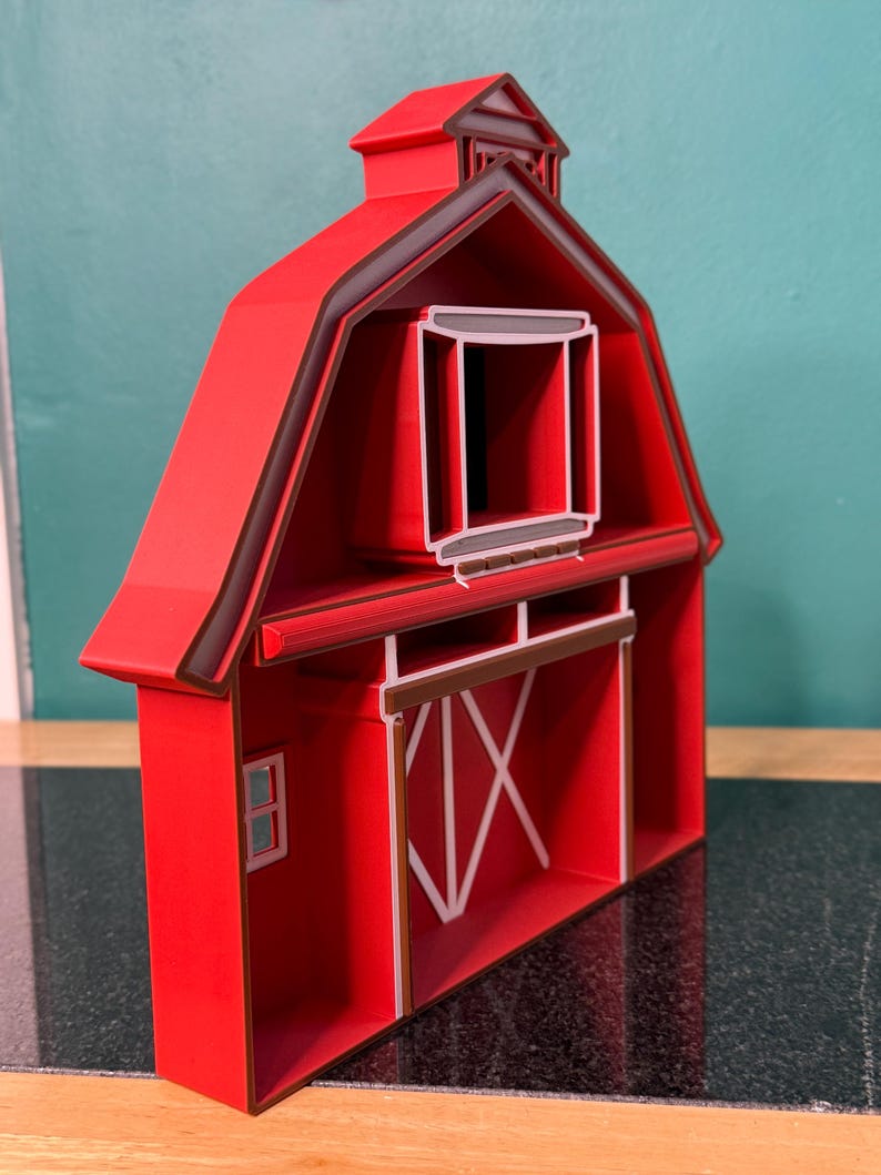 Puede incluir: Modelo de granero rojo con ribete marr&oacute;n oscuro. El granero presenta una peque&ntilde;a ventana, una gran puerta con detalles blancos y una peque&ntilde;a c&uacute;pula en el tejado. El modelo est&aacute; hecho de un material s&oacute;lido y est&aacute; dise&ntilde;ado para mantenerse en pie.