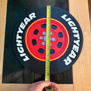 May include: A black and red Lightyear tire with the word "LIGHTYEAR" in white. The tire is being measured with a yellow tape measure, showing a diameter of approximately 32 inches.
