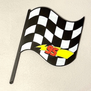 May include: A black and white checkered flag with a black pole. The flag has a yellow lightning bolt with the number 95 in red. The flag is likely a decorative item or a party decoration.