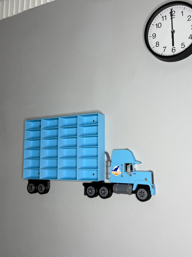 May include: A light blue toy truck-shaped wall shelf with multiple compartments. The truck has black wheels and a dinosaur logo on the side. A black and white clock is visible in the background.