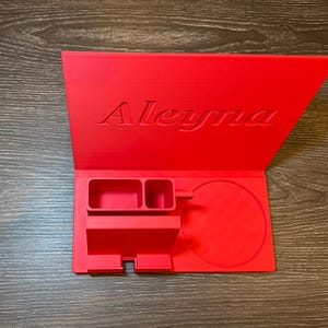 Bright red 3D-printed book stand and organiser personalised with a child’s name, designed for bedtime stories. Features sections for a cup, phone, and pens, making it a practical and fun addition to a kid’s bedside table.