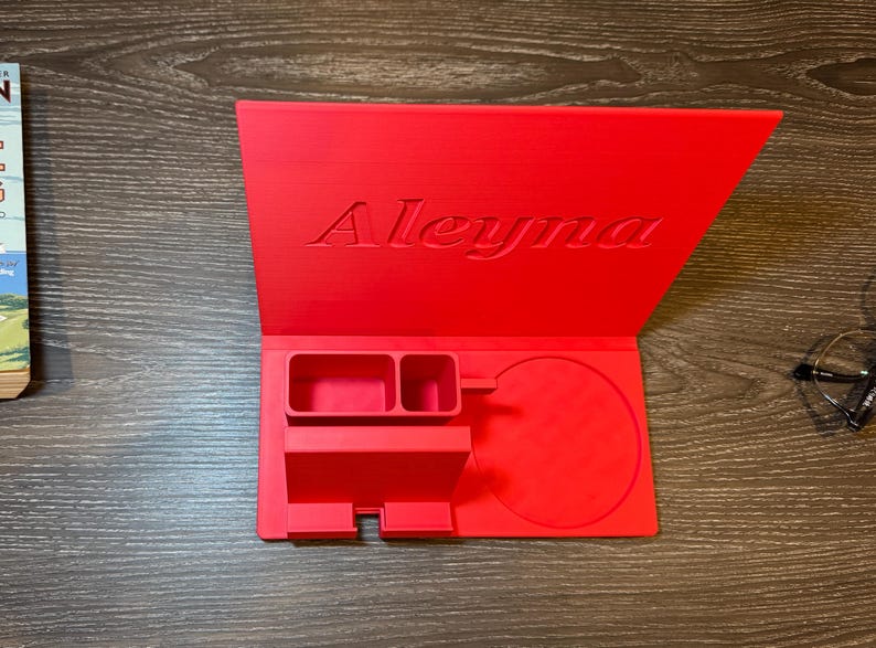 Bright red 3D-printed book stand and organiser personalised with a child’s name, designed for bedtime stories. Features sections for a cup, phone, and pens, making it a practical and fun addition to a kid’s bedside table.