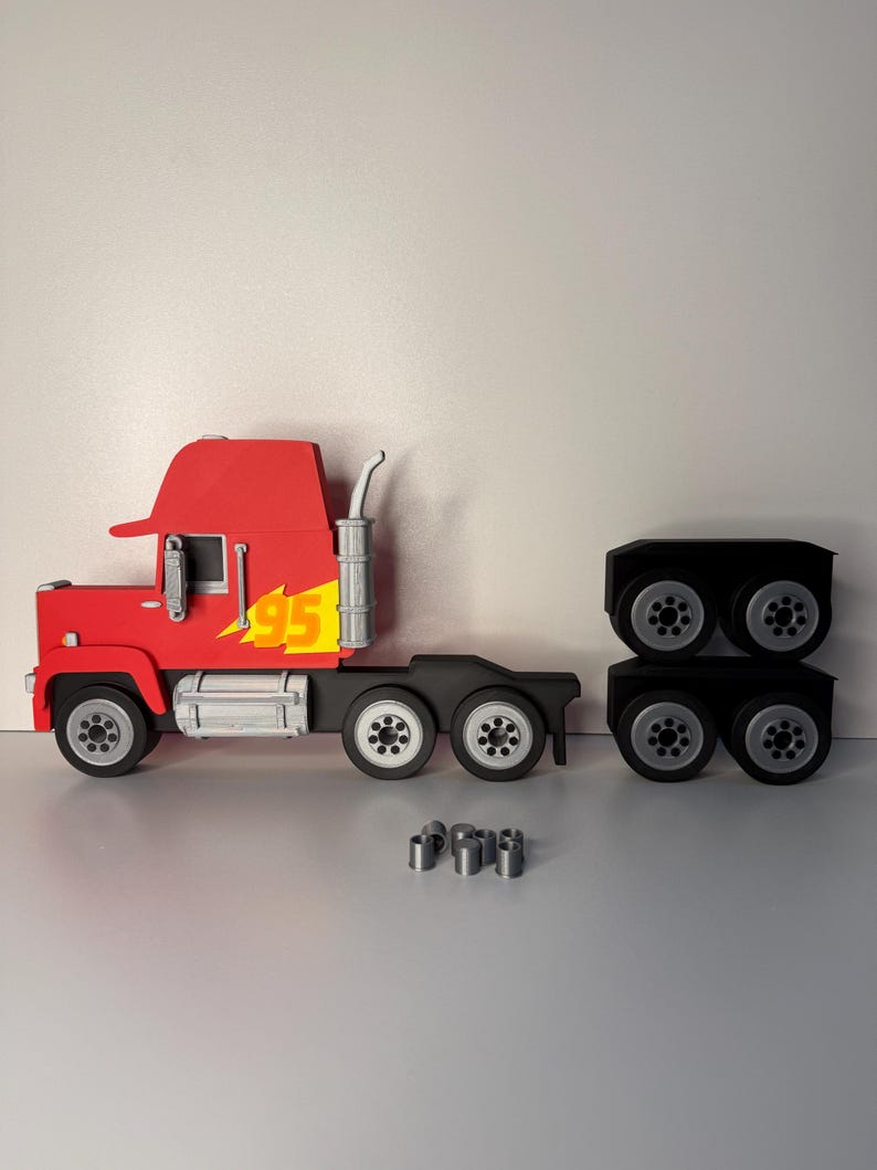 May include: A red toy semi-truck with a yellow '95' lightning bolt graphic on the side. The truck has black wheels and a silver exhaust pipe. The trailer and several silver cylinders are separate.
