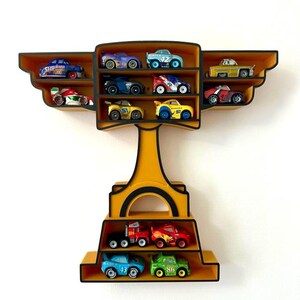 Puede incluir: Estanter&iacute;a expositora amarilla y negra con forma de trofeo, llena de coches de juguete de colores. La estanter&iacute;a tiene m&uacute;ltiples compartimentos para guardar los veh&iacute;culos en miniatura, mostrando una colecci&oacute;n de coches de carreras y camiones.