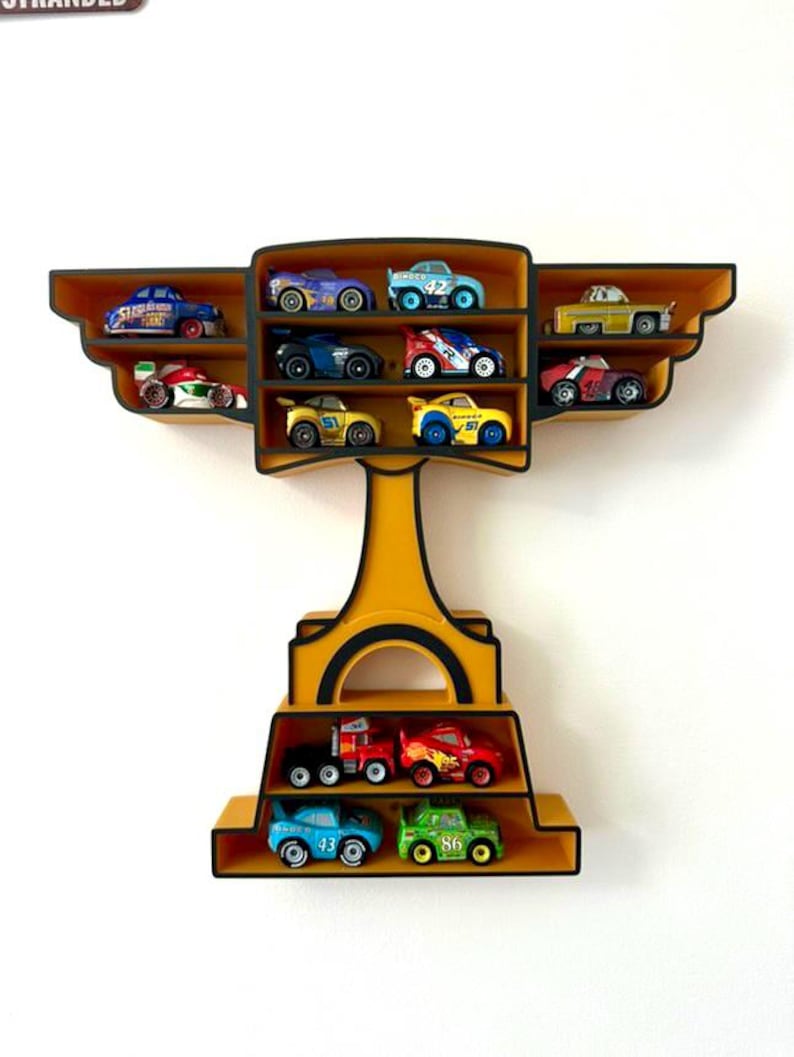 Puede incluir: Estanter&iacute;a expositora amarilla y negra con forma de trofeo, llena de coches de juguete de colores. La estanter&iacute;a tiene m&uacute;ltiples compartimentos para guardar los veh&iacute;culos en miniatura, mostrando una colecci&oacute;n de coches de carreras y camiones.