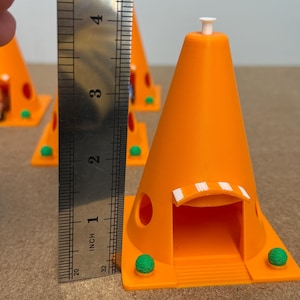 May include: Bright orange 3D-printed cone-shaped structures with a small white top and a green base. The structures are approximately 3 inches tall. The structures have a door-like opening and two green spheres on the base.
