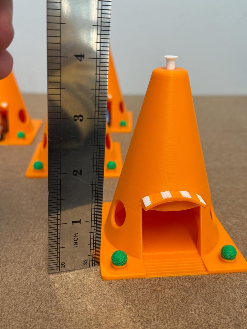 May include: Bright orange 3D-printed cone-shaped structures with a small white top and a green base. The structures are approximately 3 inches tall. The structures have a door-like opening and two green spheres on the base.