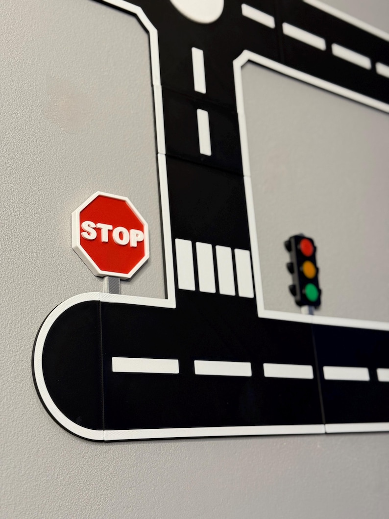May include: A black and white road sign with a red stop sign and a traffic light. The road has white dashed lines and a white border. The stop sign is red with white text.
