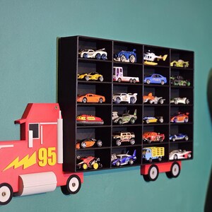 black 3D-printed truck-shaped wall shelf with red cab and yellow lightning bolt, mounted on a green wall. Holds multiple toy cars, including Hot Wheels-style vehicles. Designed for kids’ rooms or collectors. Customisable colour options available