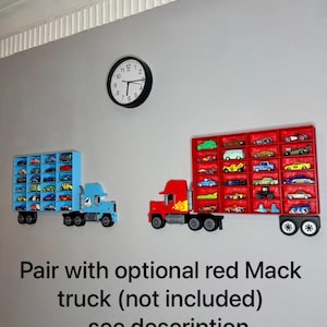 May include: Two toy truck-shaped display shelves mounted on a gray wall, one blue and one red, each filled with miniature toy cars. A black clock hangs above. The text on the wall reads "Pair with optional red Mack truck (not included) - see description."
