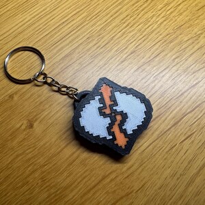 A closeup image of a 3D printed keyring, the key ring is an intentionally pixelated version of the Runecrafting skill icon from Old School Runescape OSRS. It is around 6mm thick and 40x40mm