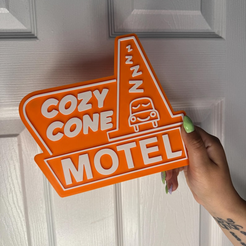 以下が含まれることがあります： オレンジと白の看板に「Cozy Cone Motel」の文字と、ZZZが書かれた漫画の車が描かれている