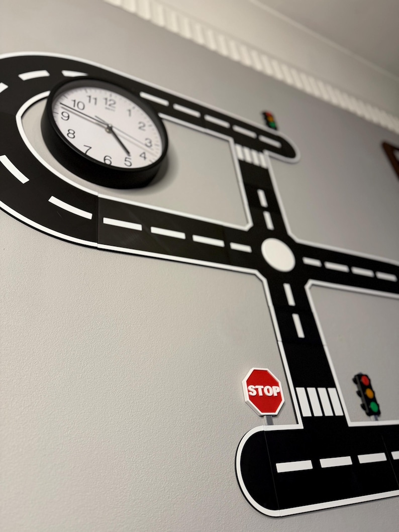 May include: A black and white road-themed wall decal with a clock, stop sign, and traffic lights. The clock has a black frame and white face. The road design includes a roundabout and crosswalk.