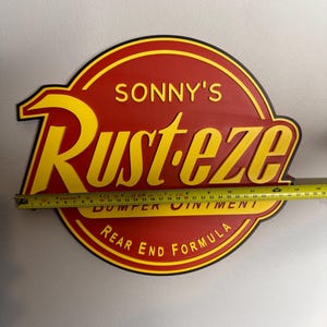 Puede incluir: Un letrero de madera rojo y amarillo con el texto "SONNY'S Rust-eze BUMPER OINTMENT REAR END FORMULA". El letrero mide aproximadamente 61 cm de ancho.
