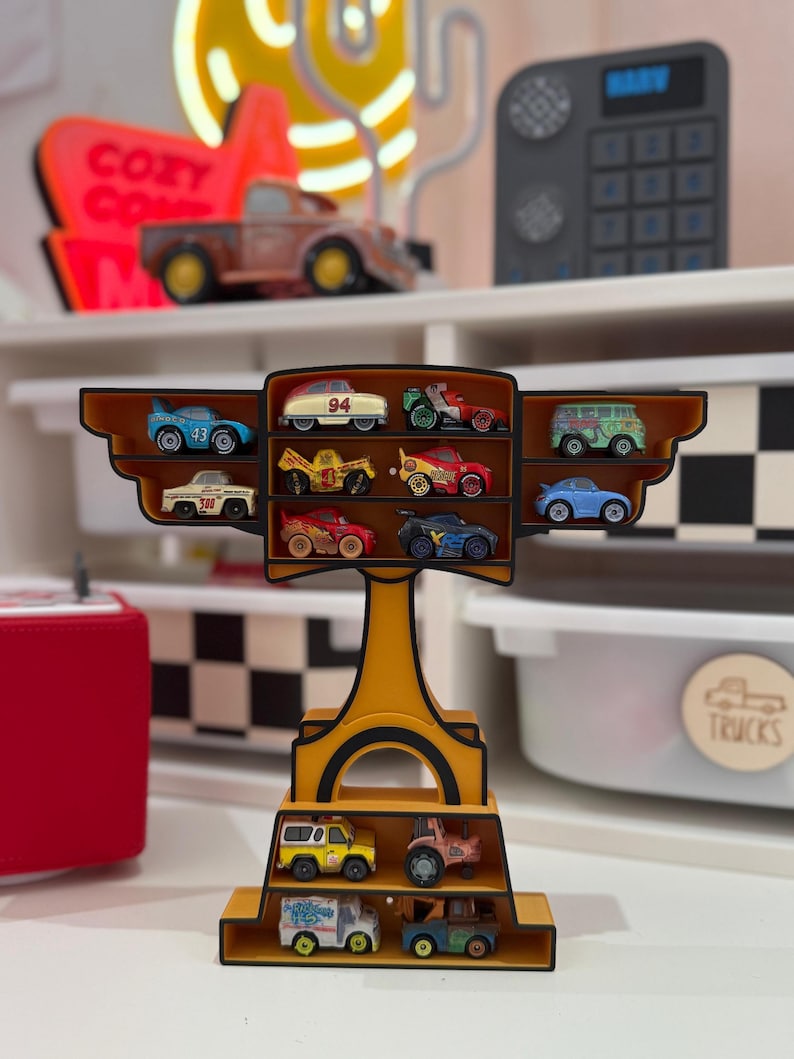 Puede incluir: Una estanter&iacute;a amarilla llena de coches de juguete en miniatura. La estanter&iacute;a tiene m&uacute;ltiples niveles y compartimentos, mostrando varios veh&iacute;culos coloridos. Los coches incluyen coches de carreras, camiones y furgonetas. La estanter&iacute;a est&aacute; decorada con un borde negro y marr&oacute;n.