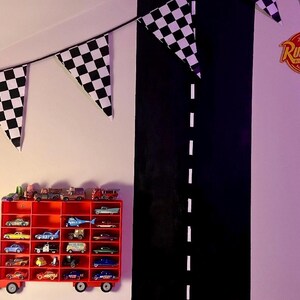 truck-shaped car shelf mounted on a themed wall, holding Hot Wheels, Disney, and Matchbox cars. The red truck design features a lightning bolt and number 95. Checkered bunting and a painted road complete the racing-themed kids’ room decor