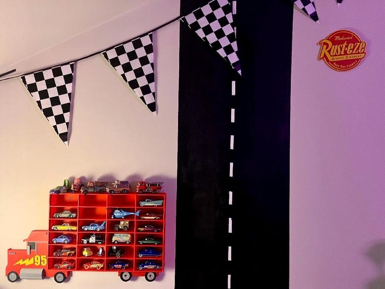 truck-shaped car shelf mounted on a themed wall, holding Hot Wheels, Disney, and Matchbox cars. The red truck design features a lightning bolt and number 95. Checkered bunting and a painted road complete the racing-themed kids’ room decor