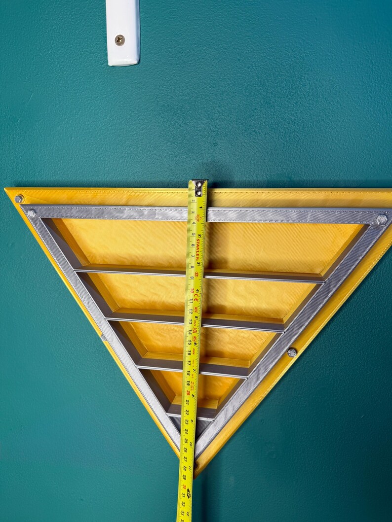 May include: A yellow triangular shelf with a silver metal frame and three interior shelves. A yellow tape measure shows the shelf is approximately 30 inches tall. The shelf is mounted on a teal wall.