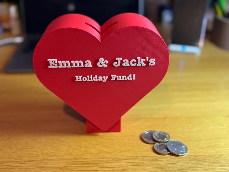 Coins for scale next to a Love heart-shaped piggy bank, ideal for saving coins, Valentine’s Day gifts, or romantic decor. A unique 3D-printed coin bank for kids or couples, perfect as a gift, decorative piece, or practical savings tool.