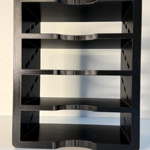 May include: A black, four-tiered organizer with a rectangular frame. Each shelf has a curved cutout in the front. The sides feature diagonal support beams. The organizer is made of a solid, matte black material.