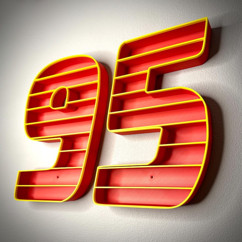 May include: A wall-mounted shelf in the shape of the number 95. The shelves are red with yellow trim. The number is mounted on a light gray wall.