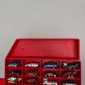 May include: A red plastic toy car display case with a hinged lid. The case has 18 slots for storing toy cars. The case is empty.