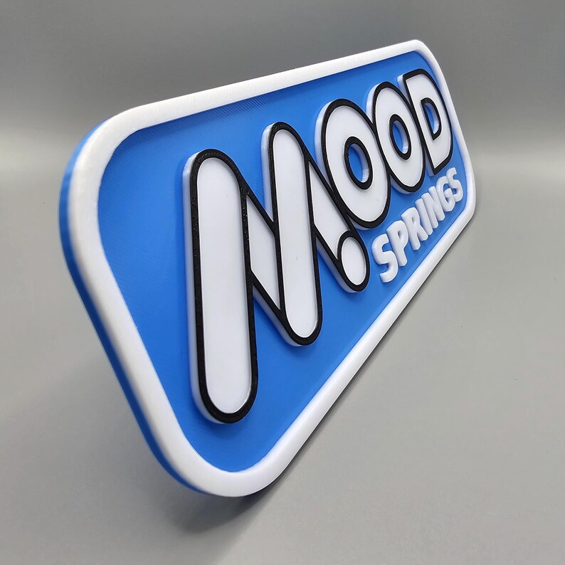 May include: A rectangular sign with rounded corners, featuring the text "MOOD SPRINGS" in white, outlined in black, against a blue background. The sign has a white border and is angled slightly.