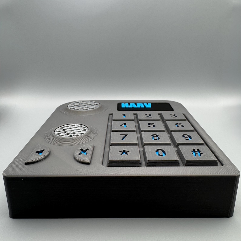 May include: A gray rectangular device with a black base, featuring a keypad with blue illuminated numbers and the text "HARV". The device has speaker and button details. The overall design is modern and functional.