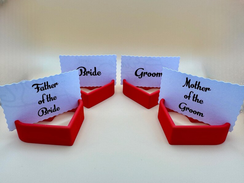 Set of 3D-printed red heart-shaped place card holders showcasing “Bride,” “Groom,” “Mother of the Groom,” and “Father of the Bride” cards. Perfect for wedding table décor.  Durable and stylish, they enhance romantic and elegant table settings.