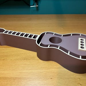 Guitar-shaped desk organiser fully assembled, with neck and body compartments for storage. 3D printed in wood-coloured PLA, resembling natural wood.