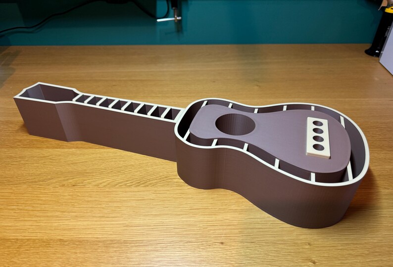 Guitar-shaped desk organiser fully assembled, with neck and body compartments for storage. 3D printed in wood-coloured PLA, resembling natural wood.