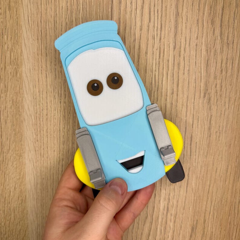 May include: A light blue, white, and brown cartoon car character with a smiling face. The character has brown eyes, a white windshield, and gray side panels. The car has a yellow bumper and a black tire.