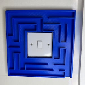 A 3D-printed, decorative light switch cover with a maze-like design. The intricate pattern adds a unique and playful touch to any room, making it both functional and visually appealing for various settings.